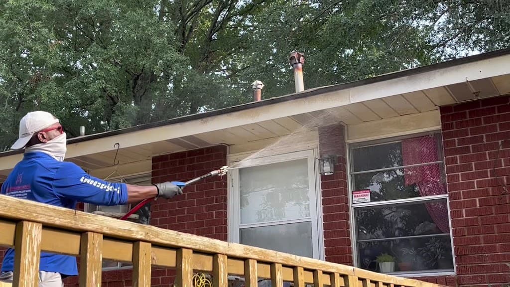 Worker soft-washing the brick eaves and soffit of a house